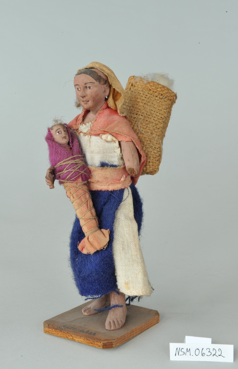 Viser kvinne med barn på armen og kurv på ryggen. Venstre arm mangler fra albuen og ned.