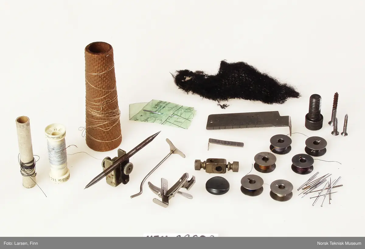 Lokket mangler. Inneholder oljekanne, verktøy, nåler, spoler, rem, symaskinfot, trådsnelle.