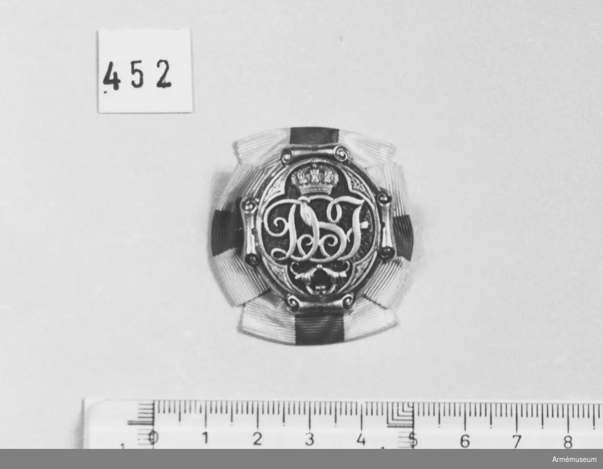 Brosch av förgylld silver och blå emalj. Med drottning Sophias initialer "D S F" krönt med en kunglig, sluten krona. Kronan är fylld med röd emalj.

Bokstävernas höjd: 14 mm. På ramen kartuscher.

På baksidan är broschnålen genomstucken ett band i rött och vitt ripsband som är förenad som en rosett och synlig från framsidan 7 mm.

På baksidan stansat "G.Möllenborg Kongl.Hovjuvelerare Stockholm.