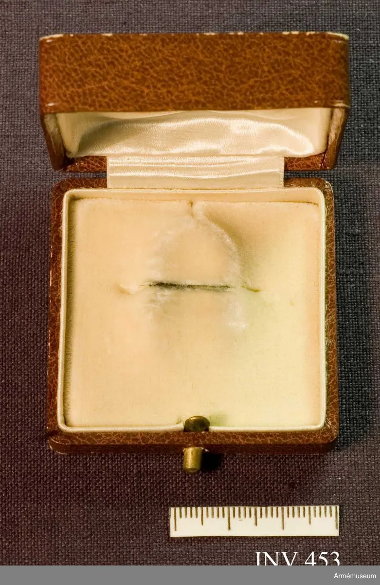 Brunt etui skänkt av fru M. Lilliehöök. Invändig botten klädd med vit sammet. Finns en springa för broschens nål. Locket invändigt klätt med vitt siden och bär en stämpel i guldtryckt: "Gustaf Möllenborg 14 Drottninggatan 14 Kongl. Hofjuvelerare. Stockholm." Över stämpeln en kunglig krona.
Samhörande nr är 452-453 och en bokgåva.
