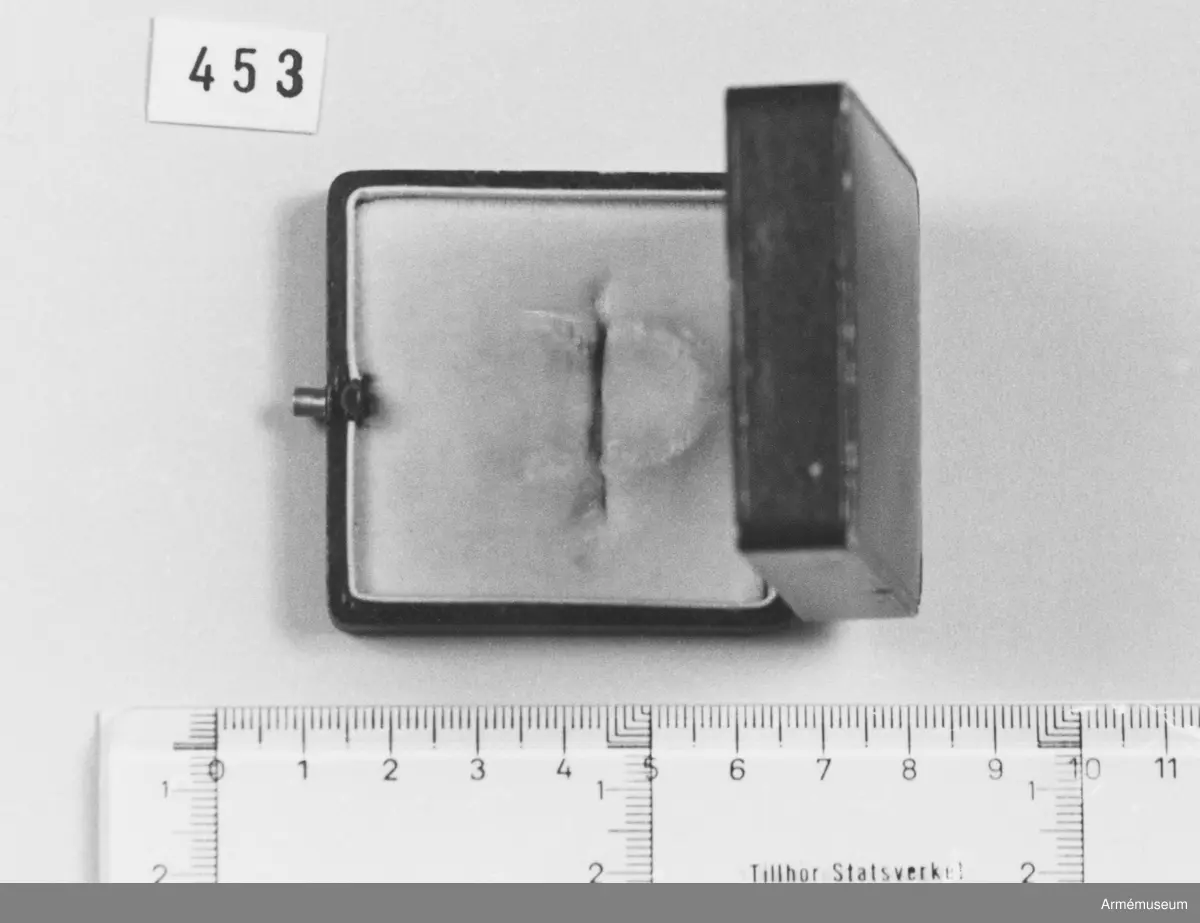 Brunt etui skänkt av fru M. Lilliehöök. Invändig botten klädd med vit sammet. Finns en springa för broschens nål. Locket invändigt klätt med vitt siden och bär en stämpel i guldtryckt: "Gustaf Möllenborg 14 Drottninggatan 14 Kongl. Hofjuvelerare. Stockholm." Över stämpeln en kunglig krona.
Samhörande nr är 452-453 och en bokgåva.