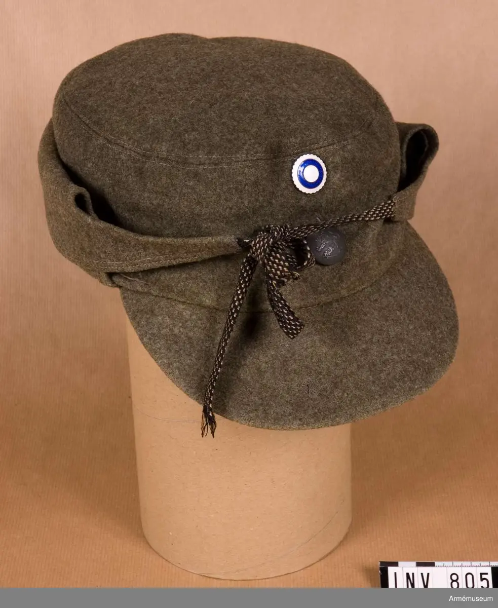 I m/1939 tygfärg. Med skärm. Nedfällbart yttre öron- och nackskydd med band för knytning. I uppfällt läge knyts banden framtill, ovan skärmen mitt fram, där det också sitter en grå knapp, m/större, med Finlandsfrivilliga Lejonet. Invändigt är kullen matelasserad. Längst fram på mössan sitter Finlands nationalitetsmärke i vitt och blått. Mössan har några malhål.
