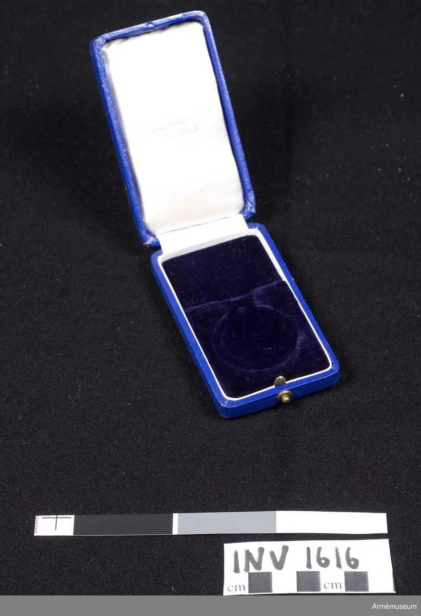 Överklädd med blålila klot. Uppfällbart lock, på insidan klätt med vitt siden med guldtext "C.C.Sporrong & CO. Stockholm". Botten invändigt klädd med lila sammet och gjord med urtag för medaljen och bandet. Knäpplås.