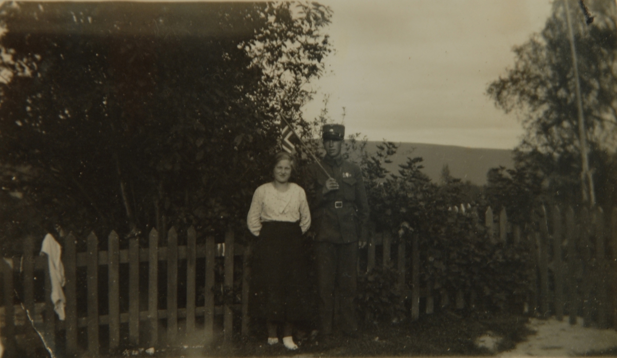 Ung kvinne og ung mann med flagg foran et stakittgjerde