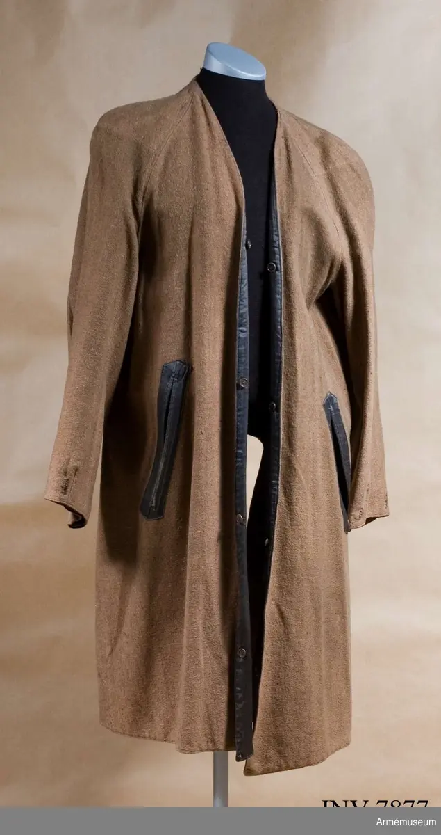 Färg brun. Ett brunt yllefoder löstagbart, fodrat med grått konstsidentyg. Försett med ficköppningar och knapphål.
På insidan finns en etikett med text: "MEA Trenchcoat Stockholm".