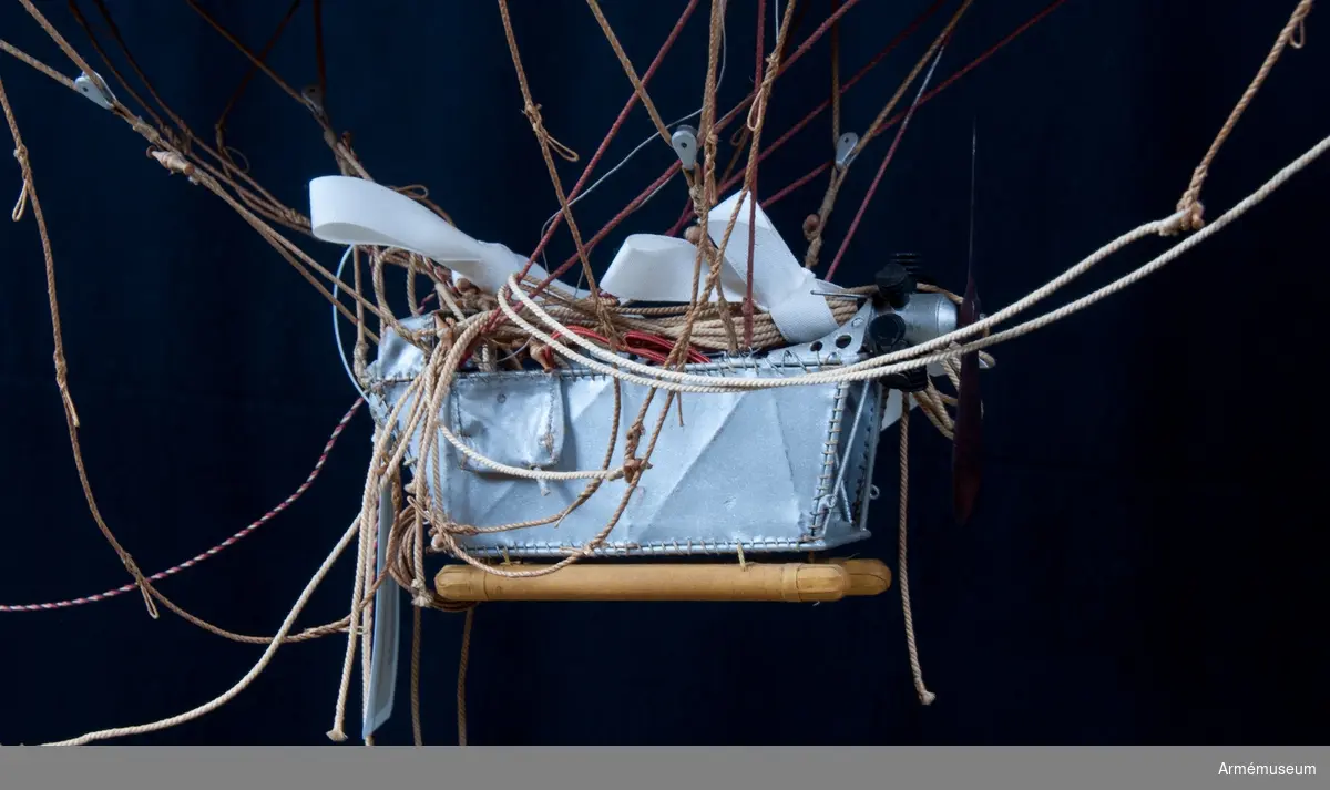 Modell av modifierad spaningsballong från ca 1928. Stora likheter med den schweiziska motoriserade M-typen av Fesselballon från samma år. Formen är långsträckt, spolformig och överklädd med gult bomullstyg av en tät kvalitet (gummiväv). Det är svårt att avgöra stommens material men det kan vara aluminium då det användes till att bygga stomme av till de "riktiga" luftskeppen. Modellen är mycket tung och därför kan det även tänkas att stommen är tillverkad av exempelvis gips. Ballongen hänger i en kraftig stålwire. Under ballongen hänger gondolen. Denna har en stomme av metall och ståltråd och är överklädd med silverfärgad väv, samt har två pontoner som "landningsställ". På ömse sidor hänger en väska. I aktern finns en propeller och på ena sidan samt mitt fram finns en ratt. Under spaningsballongens mittlinje hänger rader av linor - mitten 1 st, styrbord 4 st och babord 8 st). Dessa är mycket konstfullt utförda med s k knävringar, (styrbord 7 st, babord 10 st) fastsplitsade i ändorna. Flera linor har små öglor infästade längs med linan. Linorna är upphängda i block, - styrbord och babord har 20 st vardera. Under ballongens akter sitter balansrodret fästat varav ett roder är fast och tre är rörliga.

Se vidare Nordisk Familjebok 1912, sidan 1310, rubriken "luftskepp".