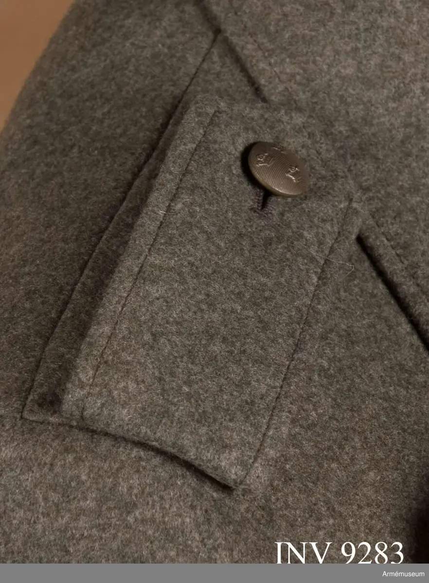 Till jacka för kvinnlig krigstjänstpersonal. Av gråbrungrönt kommisskläde med knapp och knapphål för knäppning runt tränsar på jackans axel. Axelklaffen viks  dubbel och är fodrad med gråbrunt kläde. Knapp av mindre  modellen och tillverkare Sporrong.