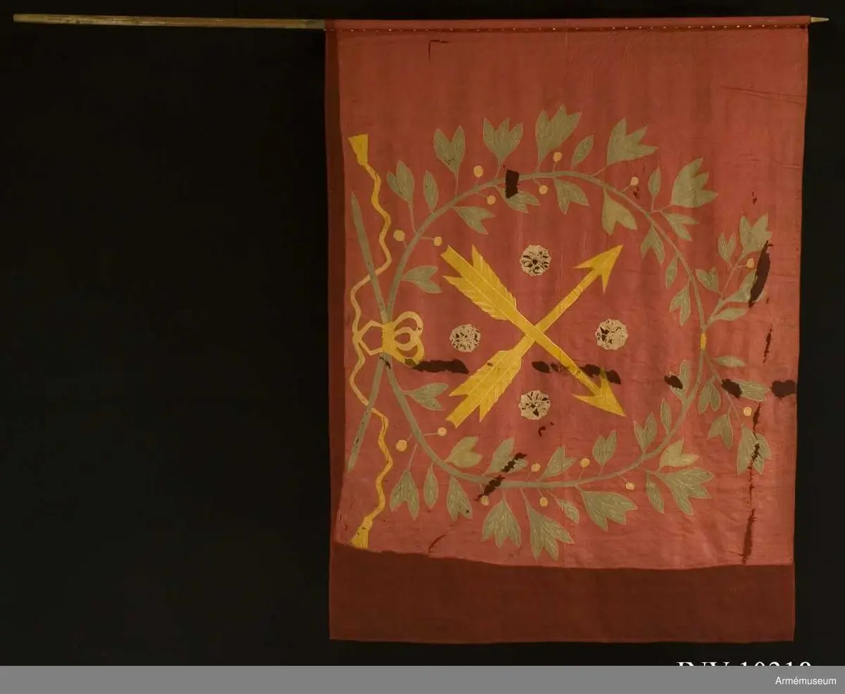 Fanduk av röd taft med insydda emblem: Närkes sköldemärke, två korslagda pilar i gult, med fyra i vinklarna ställda rosor i vitt (gulvitt), omgivet av en lagerkrans i grönt, bildad av två korslagda kvistar, nedtill hopknutna med gula band med tofsar. Skuggning och mönstring i plattsöm. Stång av vitmålad furu, senare än duken, nedtill försedd med doppsko, avbruten och försedd med två järnskenor.