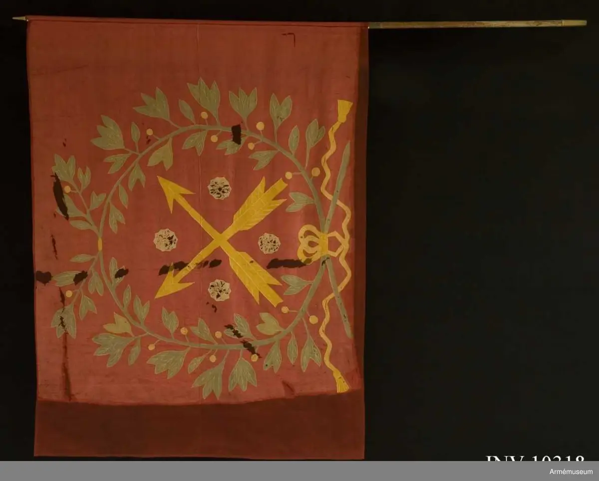 Fanduk av röd taft med insydda emblem: Närkes sköldemärke, två korslagda pilar i gult, med fyra i vinklarna ställda rosor i vitt (gulvitt), omgivet av en lagerkrans i grönt, bildad av två korslagda kvistar, nedtill hopknutna med gula band med tofsar. Skuggning och mönstring i plattsöm. Stång av vitmålad furu, senare än duken, nedtill försedd med doppsko, avbruten och försedd med två järnskenor.