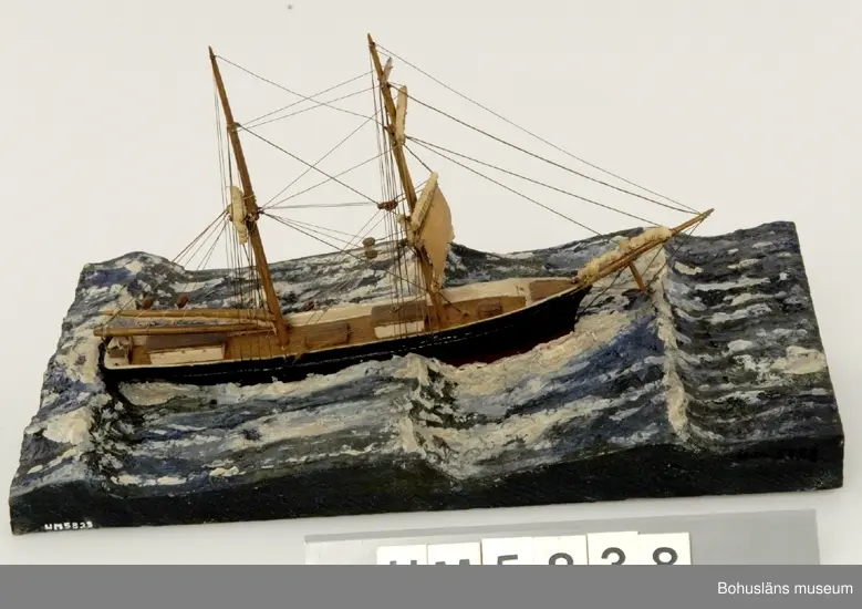 Bramsegelskonaren Beata från Helsingborg, 
Tillverkad av kapten John Emil Olsson (1880-1950), Fiskebäckskil på Skaftö i Lysekils kommun på 1940-talet.
Trä, metall, lintråd, tyg, gips.
Höjd 20 cm, längd 32 cm, B 9 cm. Platta längd 42 cm och bredd 20,5 cm. Okänd skala.
Vattenlinjemodell med två master, grönmålat skrov, röd bottenfärg, övriga detaljer vitmålade eller lackade. Stående och löpande rigg med utskurna block. Undre märssegel av snidat trä, revade segel av gasväv samt med däckshus, lastluckor och ratt. Monterad på utskuren platta med modellerad och målad gipssjö.
På plattans långsida har kapten Olsson textat med vita tryckbokstäver:
"BEATA". FRÅN HELSINGBORG 
LÄNSANDE FÖR "STOMPEN", UNDER EN SO ORKAN I NORDSJÖN (HOWDEN) NOV ÅR 1900.

Modellen föreställer hur fartyget förlorar däcklasten överbord i en orkan i Nordsjön.
I Sjöfartsbok för John Emil Olsson utfärdad vid Uddevalla Sjömanshus framgår att han var mönstrad som matros på Beata som gjorde fyra resor från Hasle på Bornholm till England via Norrland under befälhavare N. P Nilsson den 16 mars - 11 december 1901.

Definitioner:
Seglet på näst understa rån på råriggad mast kallas undermärssegel eller stump. 
Vid hårt väder beslogs fartygets alla segel utom undermärsen och man seglade "för bara stumpen". 
Blev vädret värre fick man försöka rida ut stormen och ligga bi för sviktade stumpar. Då revades halva stumpen så att bara en trekant blev kvar på rånockens ena sida.

John Emil Olsson var mönstrad på Beata  med hemmahamn Helsingborg som matros  16 mars t o m 11 december 1901 för resa  Hasle - England via Norrland (fyra resor) . 
Ur handskrivna katalogen 1957-1958:
"Beata"
Modell på platta. L. (från för till akter) 25. Föremålet helt.
Från kapten Olssons saml., Fiskebäckskil.

För ytterligare information om John Emil Olsson och förvärvet, se UM005807.

Föremålet presenterat på Bohusläns museums hemsida år 2009 - 2013, webbutställning "John Emil Olsson Fiskebäckskils sjöfartsmuseum".