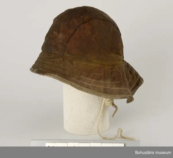 Hatt med kulle sydd i fyra längsgående stycken. Brätte som är större  
bak i nacken än framtill. Foder med öronlappar och ett snöre att knyta
under hakan. Isydd lapp anger storlek 57. Hatten är brun-röd på ut-   
sidan. Fodret är rosa.                                                
Brättet är större bak för att förhindra vatten att rinnna in vid      
nacken.                                                              

Ingår i redskapsbestånd ur sjöbod från Hällsö, Havstenssund, Tanum sn.
Se UM17521.