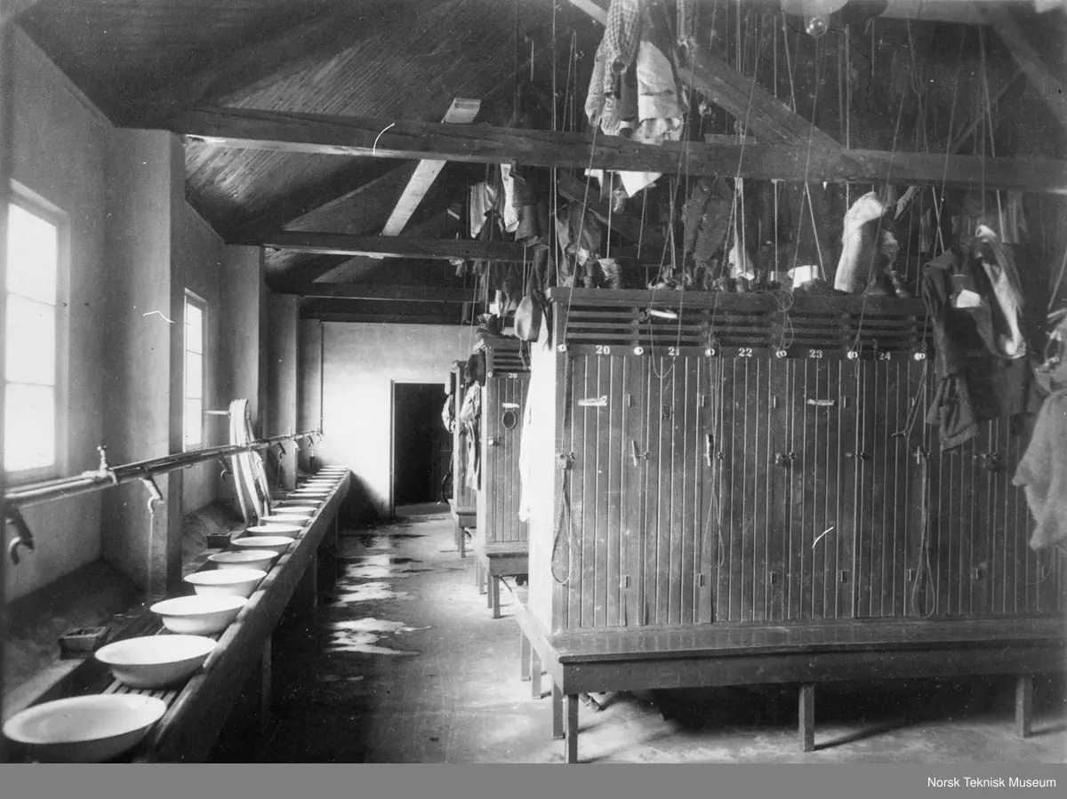 Garderobe i fabrikk med vaskevannsfat og garderobeskap. Klær henger i taket. 