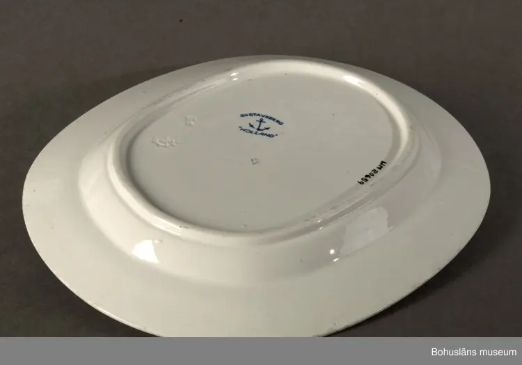 Stiliserad blå kantdekor samt tulpanliknande blomma i spegelns mitt. 
Ur servis "Holland".
Formgivare: WilhelmKåge.