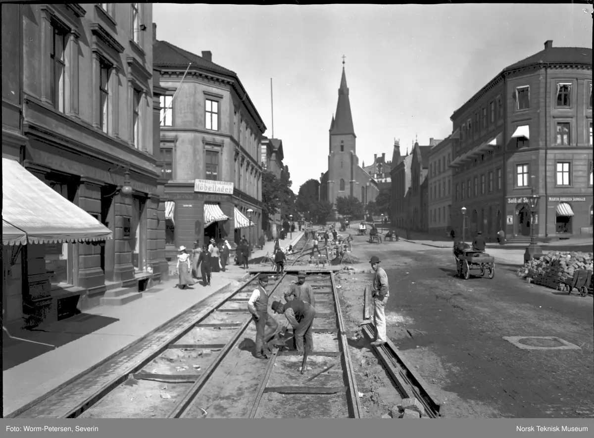 Legging av trikkeskinner i Akersgata i 1899. Bildet er tatt under arbeidet med ny sporvei fra Akersgata 18 der leseselskapet Athenæum lå, til St.Hanshaugen. St.Olavs kirke i bakgrunnen.
