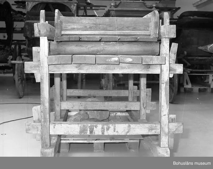 Trämangel med vagga för stenen. Två tjockare, två tunnare.
Beata Olsson  öppnade första lanthandeln i området vid Brattås, Morlanda (Henån) på 1880-talet i hus vid vägen. Mangeln uthyrdes samtidigt som lanthandeln drevs. Den var placerad i ett magasin bredvid och hyrdes av byns (Brattås) invånare. Under senare år användes den mest av
Beata Olssons släktingar. Nedmonterades något år innan den skänktes till museet.
Beata Olsson kom från Tegneby  socken. Givaren lanthandlare i Brattås.
Nuvarande affären flyttad snett över vägen längre ned i backen.