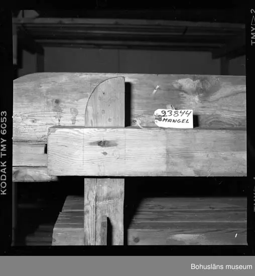 Trämangel med vagga för stenen. Två tjockare, två tunnare.
Beata Olsson  öppnade första lanthandeln i området vid Brattås, Morlanda (Henån) på 1880-talet i hus vid vägen. Mangeln uthyrdes samtidigt som lanthandeln drevs. Den var placerad i ett magasin bredvid och hyrdes av byns (Brattås) invånare. Under senare år användes den mest av
Beata Olssons släktingar. Nedmonterades något år innan den skänktes till museet.
Beata Olsson kom från Tegneby  socken. Givaren lanthandlare i Brattås.
Nuvarande affären flyttad snett över vägen längre ned i backen.