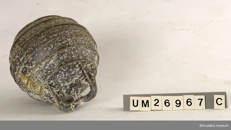 Fem klotformade flöten av metall (aluminium eller zink?). Beskrivningar av flötena i storleksordning följer här:
1. Omkrets 64 cm, med tre upphöjda ränder runtom på mitten och korta upphöjda ränder på tvären mellan dem på några ställen. I utstickande rektangulär del med rundade hörn finns två runda hål bredvid varandra. Text i relief: MANUFACTURERS PHILIPS ...(Oläsligt) TRAWL PRODUCTS GRIMSBY? ENGLAND ? (Svårlästa ord). Oläslig text p g a att den är bortsliten även på ytterligare ett ställe. Slitet.
2. Omkrets 63,5 cm, med sju upphöjda ränder, den mittersta bredare än de övriga. Två rundade metallöglor med gemensam mittdel sticker ut. Text i relief: AUTRIEB ? (Svårläst)...(Oläsligt) Märke som ser ut som ett kantigt stort S och siffrorna 197. Mycket smutsigt, fläckvis vit beläggning.
3. Omkrets 63 cm, slät yta utan upphöjningar, målad i vitaktigt grönblått i två olika nyanser, färgen delvis avsliten. Utstickande del med två närmast fyrkantiga hål. Text i relief: ... (Oläsligt ord) DE ... (Oläsligt ord) PARIS. Stor rostfläck. Mycket slitet.
4. Omkrets 55,5 cm. Med fem upphöjda ränder runtom. Rundad del med två kvartcirkelformade hål sticker ut. Text i relief: MADE IN SPAIN LA CORONA, bild av en fyr med ljusstrålar samt patentnummer med 39 siffror i. Samma? text/bild/siffror finns på ytterligare ett ställe fast är där mer sliten. Slitet.
5. Omkrets 37 cm. En upphöjd rand på mitten, för övrigt slät yta. En ögla sticker ut på ett ställe. Knutet runt den finns rester av snöre. Slitet. Rostfläckar m fl fläckar.

För uppgifter om brukaren se UM026962
Se även Bohusläns museums arkiv, arkivnummer 389.
