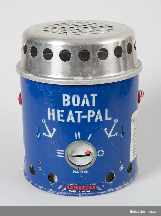 Rund kamin, värmare  av märket "BOAT HEAT-PAL".Underdel av blålackerad metall med brännre för blåsprit eller T-sprit. Överdel med genombruten skyddskåpa.
Genom att lyfta av överdelen kan värmaren även användas som ett litet kök för ett kärl på gallret.
Bärrem av kraftigt vävt band i rött-vitt och blått.
Fastkklistrade etiektter med instruktioner och säkerhetsföreskrifter
Korroderad.