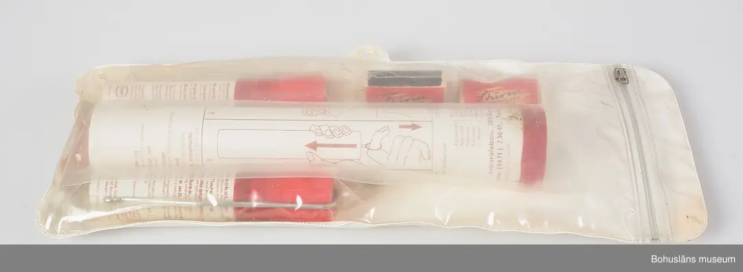 Plastförpackning med nödsignaler innehållande en större fallskärmssignal och två mindre handfacklor och två askar med stormtändstickor, allt i separata plastförpackningar. Försluts med dragkedja av plast. 
På baksidan tryckt text:
KEEP DRY
It is essential that these signals be inspected frequently and
kept dry. These packs afford good protection but should not
be expected to withstand prolonged immersion in water."
På föremålen beskrivs användnng i bild och text.