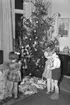 Tre förväntansfulla barn väntar på julklappsutdelning, december 1949