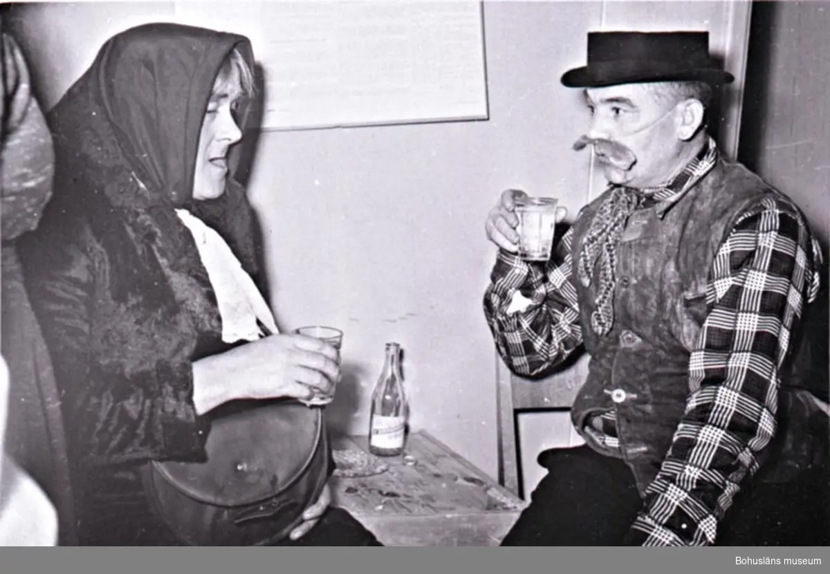 Luciafirande på konservfabrik omkring 1950. Två män i maskeradkläder, utklädda som äldre man och gumma, sitter vid ett bord och skålar med varandra.