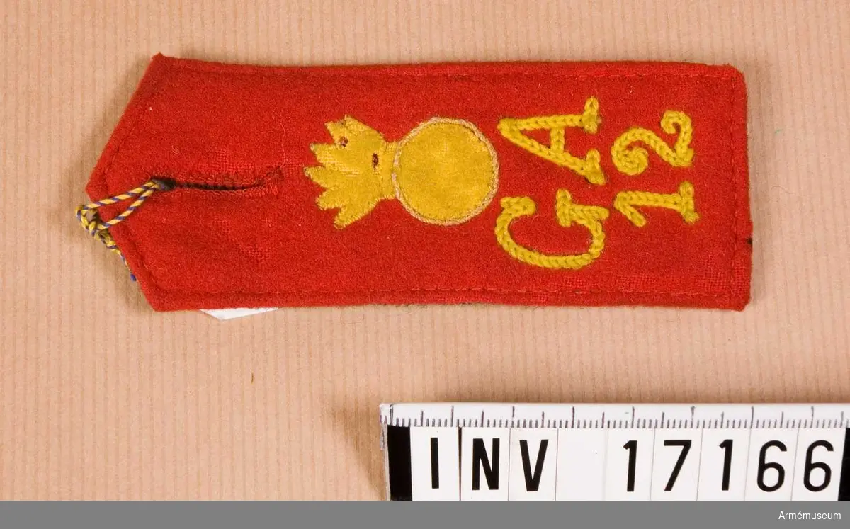 Grupp C I.
Axelklaff för manskap vid artilleriregementet von der Goltz under frihetkriget i Finland 1917-1918. Axelklaff av rött kläde, 4 cm bred med broderat "G.A. 12" - troligen: Gebirge artilleriet N 12 regementet. Ovanpå initialer - emblem granaten (artilleritecken). Foder av grått kläde. General v. der Goltz armé har kommit år 1918 till Finland för att hjälpa Finlands vita armé att bekämpa de röda.