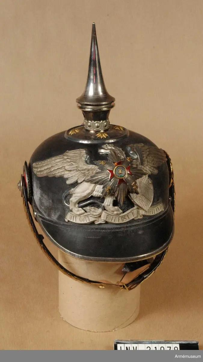 Grupp C I.
Ur uniform för officer vid Badisches Leibgrenadierregiment. Består av kappor, kolletter, syrtut, vapenrock, ridbyxa, långbyxor, hjälm, mössa, skärp, sabel m tillbehör.
Hjälm av svart lackerat läder med fram och bakskärm, avrundade. Framskärmen har beslag av vit metall. På hjälmens baksida finns en skena, som går från spetsen till nacken. Alla hjälmens metalldelar består av nysilver utom hakremmen som är av fjäll, s.k. tomlach. Foder av vitt skinn och siden med krona. Hakremmar av läder med ciselerade fjäll med rosetter av nysilver samt ett spänne. Kokarder: på hjälmens H sida under hakremsrosetten en svart- vit-röd =tyska nationalfärger. På V sida en gul-röd  =Badenska färger. Rikskokarden med ring av nysilver =officers tecken. Vapenplåt på framsidan med heraldiskt, badenskt vapen med stjärna.
Enl W Granberg.