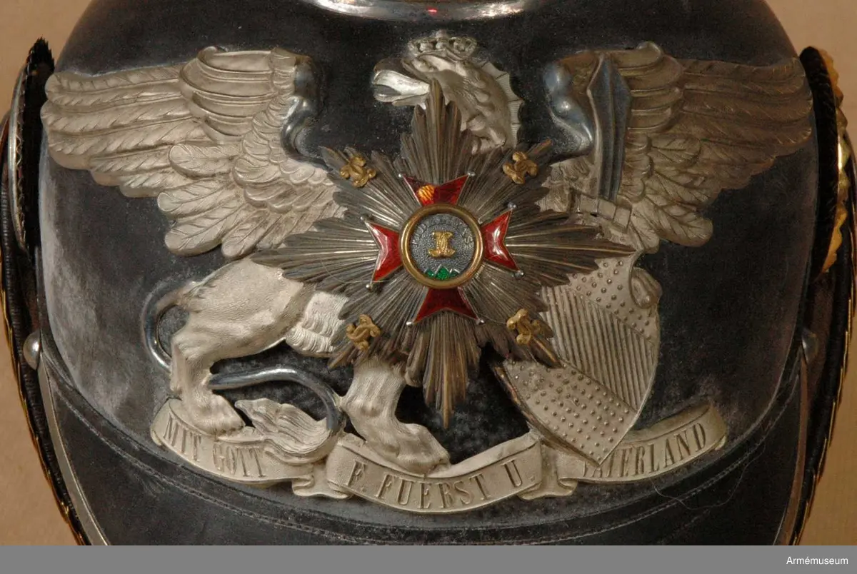 Grupp C I.
Ur uniform för officer vid Badisches Leibgrenadierregiment. Består av kappor, kolletter, syrtut, vapenrock, ridbyxa, långbyxor, hjälm, mössa, skärp, sabel m tillbehör.
Hjälm av svart lackerat läder med fram och bakskärm, avrundade. Framskärmen har beslag av vit metall. På hjälmens baksida finns en skena, som går från spetsen till nacken. Alla hjälmens metalldelar består av nysilver utom hakremmen som är av fjäll, s.k. tomlach. Foder av vitt skinn och siden med krona. Hakremmar av läder med ciselerade fjäll med rosetter av nysilver samt ett spänne. Kokarder: på hjälmens H sida under hakremsrosetten en svart- vit-röd =tyska nationalfärger. På V sida en gul-röd  =Badenska färger. Rikskokarden med ring av nysilver =officers tecken. Vapenplåt på framsidan med heraldiskt, badenskt vapen med stjärna.
Enl W Granberg.