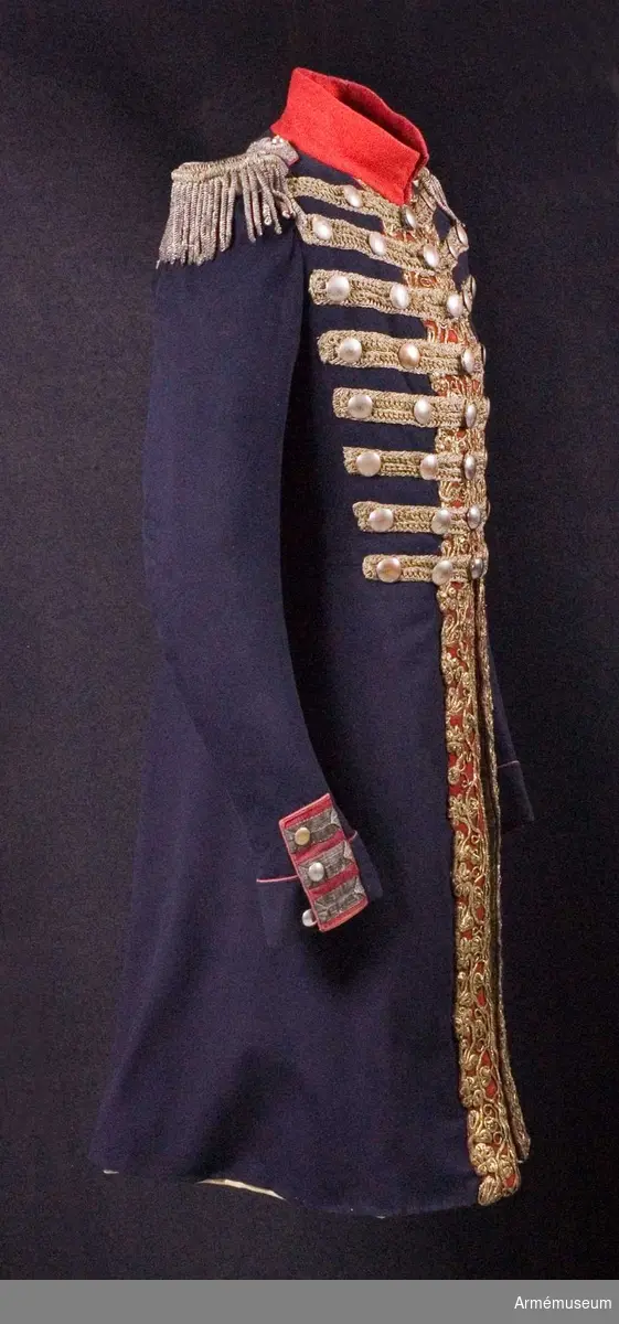 Blå knälång rock med röd krage och snörmakerier av förgylld metalltråd.
Renoverad och försedd med nya ärmuppslag omkring 1831.

Rocken är sydd av fint mörkblått kläde och har snörmakerier av guldlan fastsydda på en remsa av rött kläde på båda sidor om knäppningen mitt fram, samt i slitsen bak. Dessutom revärer över bröstet utförda av förgyllda tvinnade metallsnoddar, och 5 rader med 8 rent dekorativa knappar i varje rad. Knapparna är släta och svagt välvda, och av en försilvrad kopparlegering. Den egentliga knäppningen är 2 x 7 hyskor och hakar kant i kant mitt fram, samt 2 x 2 dito i kragen.
Rocken är konstruerad med fram- och sidstycken i ett, samt helt bakstycke utan söm mitt bak. Den har midjesöm med separat skört. Skörtet har fram- och sidstycken i ett, och två smalare bakstycken vid slitsen bak. Röd ståndkrage av fint kläde, fodrad med det samma.
Ärmarna är formade tvåsömsärmar med fasta ärmuppslag med smal röd passpoal och röd matta med tre "knapphål" av metallgalon som pryds av tre mindre knappar.
De svängda sidsömmarna bak är dekorerade med samma förgyllda tvinnade metallsnoddar som revärerna. Vid ryggslutet sitter två knappar.
Bålen är fodrad med gråvitt fint ylletyg, medan ärmarna är fodrade med oblekt eller vitt linne.

Till rocken hör ett par epåletter av silvergalon med fransar av krusade och vridna silvertrådar.