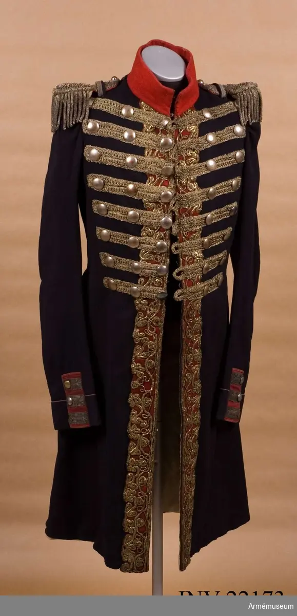 Blå knälång rock med röd krage och snörmakerier av förgylld metalltråd.
Renoverad och försedd med nya ärmuppslag omkring 1831.

Rocken är sydd av fint mörkblått kläde och har snörmakerier av guldlan fastsydda på en remsa av rött kläde på båda sidor om knäppningen mitt fram, samt i slitsen bak. Dessutom revärer över bröstet utförda av förgyllda tvinnade metallsnoddar, och 5 rader med 8 rent dekorativa knappar i varje rad. Knapparna är släta och svagt välvda, och av en försilvrad kopparlegering. Den egentliga knäppningen är 2 x 7 hyskor och hakar kant i kant mitt fram, samt 2 x 2 dito i kragen.
Rocken är konstruerad med fram- och sidstycken i ett, samt helt bakstycke utan söm mitt bak. Den har midjesöm med separat skört. Skörtet har fram- och sidstycken i ett, och två smalare bakstycken vid slitsen bak. Röd ståndkrage av fint kläde, fodrad med det samma.
Ärmarna är formade tvåsömsärmar med fasta ärmuppslag med smal röd passpoal och röd matta med tre "knapphål" av metallgalon som pryds av tre mindre knappar.
De svängda sidsömmarna bak är dekorerade med samma förgyllda tvinnade metallsnoddar som revärerna. Vid ryggslutet sitter två knappar.
Bålen är fodrad med gråvitt fint ylletyg, medan ärmarna är fodrade med oblekt eller vitt linne.

Till rocken hör ett par epåletter av silvergalon med fransar av krusade och vridna silvertrådar.