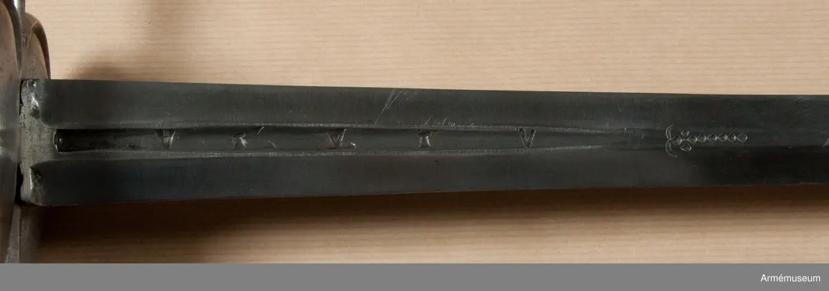 Klingan är tveeggad med flata åsar. Upptill på var sida har den en blodrand, som på yttersidan är 16,5 cm lång. Under den nedra ändan på varje blodrand finnes ett av prickar bestående onament.

Fästet är av polerat järn och av drabanttyp. Knappen är svagt ellipsiodisk med rygg fram och bak. Diam. sidled är 3,95 cm, men över ryggarna 4,15 cm. Höjden är 4,3 cm. Nitknappen är låg och närmast cylindrisk. Halsen är ävenledes låg med konisk. Höjden av hals, knapp och nitknapp är sammanlagt 5,25 cm. 
Kaveln är spolformig med flat rand fram och bak, men sidorna är avrundade. Upp- och nedtill omgives den av en ringliknande, platt flätning, "krans", av rätt varierande bredd, i huvudsaken dock 0,7 cm, vilken flätning består av mässingstråd, men är hopsnodd av två parter. I övrigt är kaveln lindad med 4 mässingstrådar, av vilka två är rätt grova, den ena höger- den andra vänstersnodd, men de båda övriga rätt fina.
Parerstången är nästan rak och blir mot ändarna litet bredare. Den främre änden är avrundad, men den bakre har mer tvär avslutning. Armarna ha spetsovalt tvärsnitt. Den största bredden är för den främre armen 1,1 cm, men för den bakre 1,25 cm. Den största tjockleken är för bägge armarna 0,85 cm. Avståndet mellan den främre eggen och parerstångens främre ändan är 6,8 cm, men mellan den bakre eggen och den bakre änden 5,9 cm. 
Parerplåten är hjärtformig och har förhöjda kanter, vilka sistnämda egentligen bestå av spänger, en på var sida, vilka från parerstångens bakre arm gå till handbygelns nedre del. Tomrummen mellan spängerna och parerstången, resp. handbygelns nedre del, ha utfyllts med ett par kupiga plåtar, som faslötts med mässing. Parerplåten är något större på ytter- än på insidan. Avståndet mellan klingans mitt och parerplåtens kant är på det förstnämda stället 4,6 cm, men på det sistnämda 4,5 cm. 
Handbygeln utgår från korset, har spetsovalt tvärsnitt och den största bredden litet ovanför parerplåtens spets. Dess övre ända är instucken i ett hål i knappen. På handbygelns innersida nära övre ändan är bokstäverna AD inslagna. Tumbygel finnes icke.