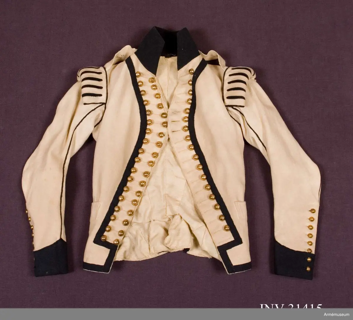 Jacka m/1792, av vitt kläde med hög krage, passpoaler, ärmuppslag och andra detaljer i mörkblått kläde.
Plagget är kraftigt svängt mitt fram, knäppt med tre knapprader med 18 guldfärgade klotknappar i varje rad, varav bara de 3 på mitten går att knäppa. Övriga knapphål är stumma.
Vid axeln finns stoppade axelkarmar av vitt kläde med slitsar fodrade med blått kläde. Här finns även fastsydda axelklaffar av enkelt vitt kläde med en blå stjärna applicerad. Axelklaffarna fästs ner med en enkel klotknapp av samma typ som övriga.
Ärmarna är tvåsömsärmar med blå passpoaler i båda sömmarna och sprund längst ner på ärmen som knäpps med 8 mindre kulknappar i varje. I höger ärm saknas en knapp längst ner.
Två grunda horisontella fickor. Litet skört bak.
Jackan är fodrad med fint kypertvävt ylletyg i bålen, men med tuskaftvävt linne- eller hampatyg i ärmarna.