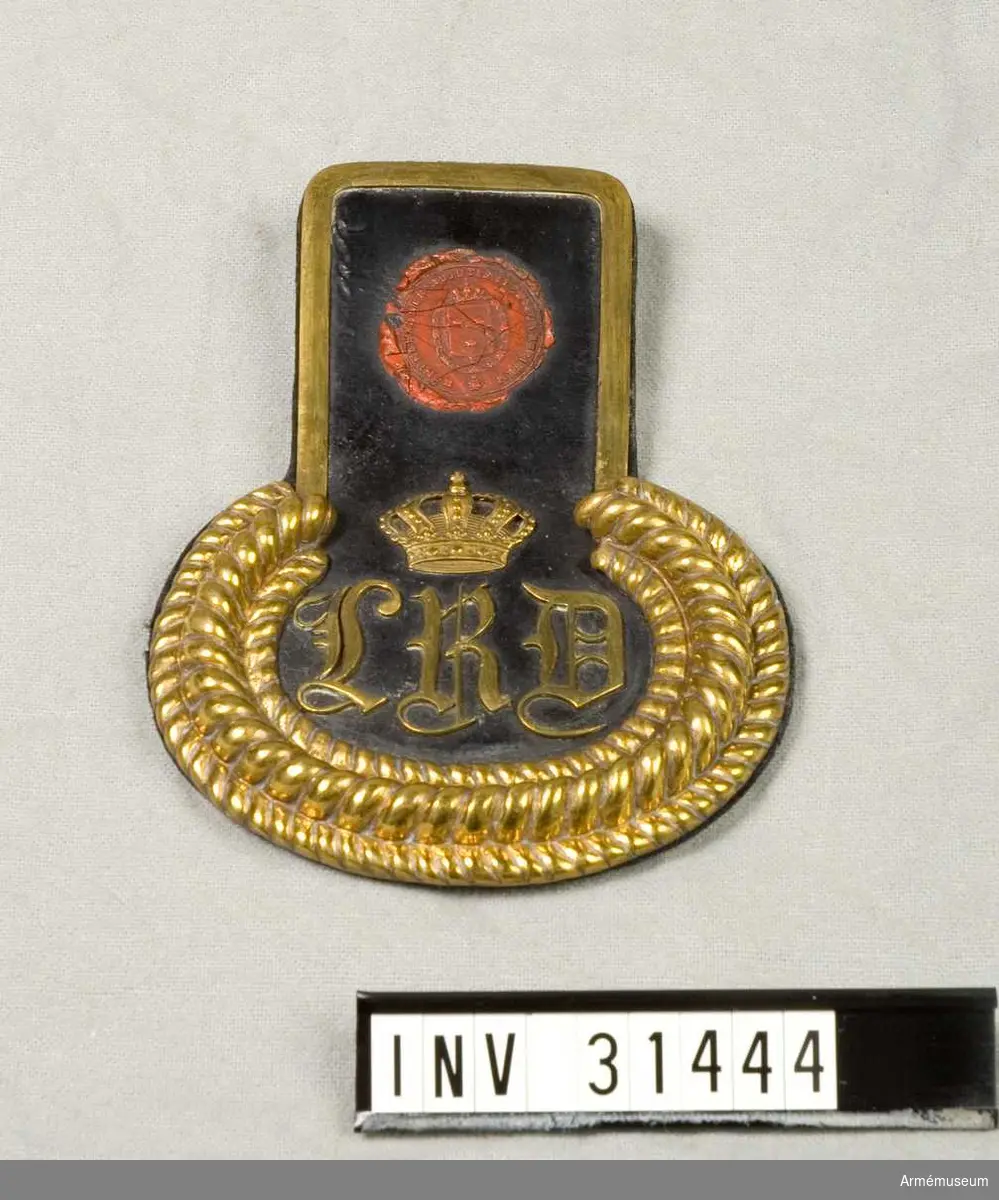 Epåletter av svart läder med mässingsbeslag. Bokstäverna "L. R. D.".

Modelletikett med text: "Af Kongl. Majt Nådigst faststäldt modell å Epauletter för Lif Regts Dragon Corps, enl. General Adjutantens för Armén Skrifvelse d. 30. sistl. Augusti. Stockholm d. 24. November 1823. På Befallning T. W. Lode. Adjut. i Kgl. Krigs Colleg." Baksidan: "Denna Modell är icke vidare gällande sedan Kungl. Majt under den December 1845. i Nåder fastställt nya Modeller å Beklädnadspersedlar för denna corps, hvartill Epauletter för manskapet icke begagnas."