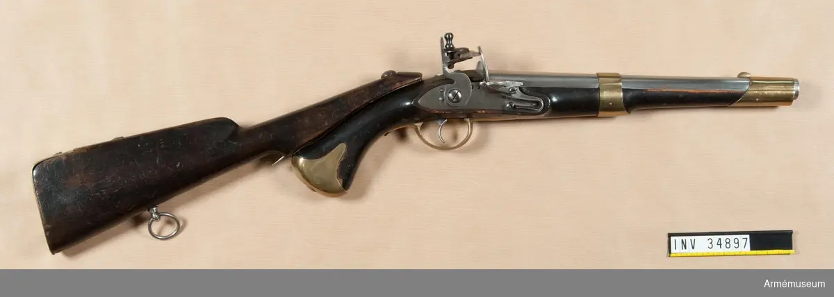 Pistol med flintlås.
Studsarpistol m/1807 (1806?) av Helvigs konstruktion. Längd med påsatt löskolv: 712 mm. Pipan är rund. Svansskruven har baktill en hake, som är inpassad i ett hål i det vid stocken fästa svansjärnet. Ett högt, båtformigt mässingskorn sitter 4,2 cm bakom mynningen. På svansjärnet sitter ett högt ståndsikte. Svansjärnet fasthålls av en uppifrån isatt korsskruv. På pipans översida krönt N T (Norrtälje), på undersidan ett P och på vänstra platten en otydlig stämpel. På svansjärnet en otydlig kronstämpel. Loppet har 4 spiralräfflor.

Låset har platt bleck, fängpannearm och eldskärm. Studeln har en egendomlig, kantig form. Slag och eldstålsfjädrarna är så krökta att främre låsskruven går inom deras bukter. pannskruven går inifrån, men skruven för eldstålsfjädern utifrån. På bleckets utsida under eldstålsfjädern ett S, på insidan siffran 2 och en otydlig kronstämpel.

Stocken är av björk och svart, till vänster om varbygeln främre arm en otydlig stockmakarestämpel och till höger om denna arm spår av rött lacksigill. Ovanför sidblecket är inslaget numret 16. Beslagen är av mässing. Kolvkappan har rätt korta, avrundade flikar och är hoptryckt från sidorna. Den fasthålls av en skruv i centrum. Varbygelns bakre arm går ned till kolvkappan och är fäst med en skruv. Den korta främre varbygelsarmen har docka. Sidblecket är platt och böjt i rät vinkel. Pipan fasthålls av två band, vilka kvarhålls av stift. Näsbandet är upptill utskuret för kornet och har nedtill en kort, bakåtgående spets. Det andra bandet har nedtill en kort framåtriktad spets. På sidblecket, näsbandet och kolvkappan inslaget G S. På varbygelns bakre arm en stämpel med ett monogram av A.L.

I kolvens övre sida är ett kraftigt "anslagsjärn" infällt och till ungefär 1 cm från svansjärnets bakände. fasthålls av fyra skruvar. Anslagsjärnet går från kolvkappan till ungefär 1 cm från svansjärnets bakände. Längst ned vid kappan finns i järnet ett runt hål och omkring 8 cm längre upp har det ett avlångt hål.

Löskolven är svart, av björk och har bakplåt av mässing. Löskolvens "hals" är avsneddad på undersidan så att den där noga passar till pistolkolves översída. I detta avsneddade parti är "häftjärnet" infällt och fasthålls av tre skruvar. En bit nedanför häftjärnets överkant sitter "häfttappen". Denna består närmast häftjärnet av en omkring 6 mm hög, cylindrisk tapp med 7 mm diameter. På denna tapp sitter ett rektangulärt, 13 mm långt, 5 mm brett och 5 mm högt ax på tvären med häftjärnet längdriktning. På insidan av häftjärnets är en lång "häftfjäder" placerad. Häftfjädern sticker nedtill ut omkfing 1,7 cm nedanför häftjärnets bakände. Litet ovanför denna bakände genombryts häftjärnet av ett hål, genom vilket en på häftfjädern sittande tapp utsticker.

När man påsätter löskolven, inpassar man häfttappen i anslagsjärnets övre hål, vrider löskolven åt vänster och trycker in häftfjäderns utstående del. Då anslagsjärnet och häftjärnet ligger på varandra, släpper man häftfjädern, varvid häftfjäderns tapp drivs ned i anslagsjärnets runda hål samt sålunda fastlåser löskolven vid pistolen. Därigenom kunde man skjuta med pistolen stödd mot axeln alldeles som med ett gevär. Ett par pistoler av denna modell består av en studsarepistol, lika den som ovan beskrivits, och en slätborrad blänkare- eller flankörpistol (se AM 4780). Till varje pistolpar hördes en löskolv, också kallad "löst anslag", och en lös laddstock. Löskolven och laddstocken passade till bägge pistolerna.