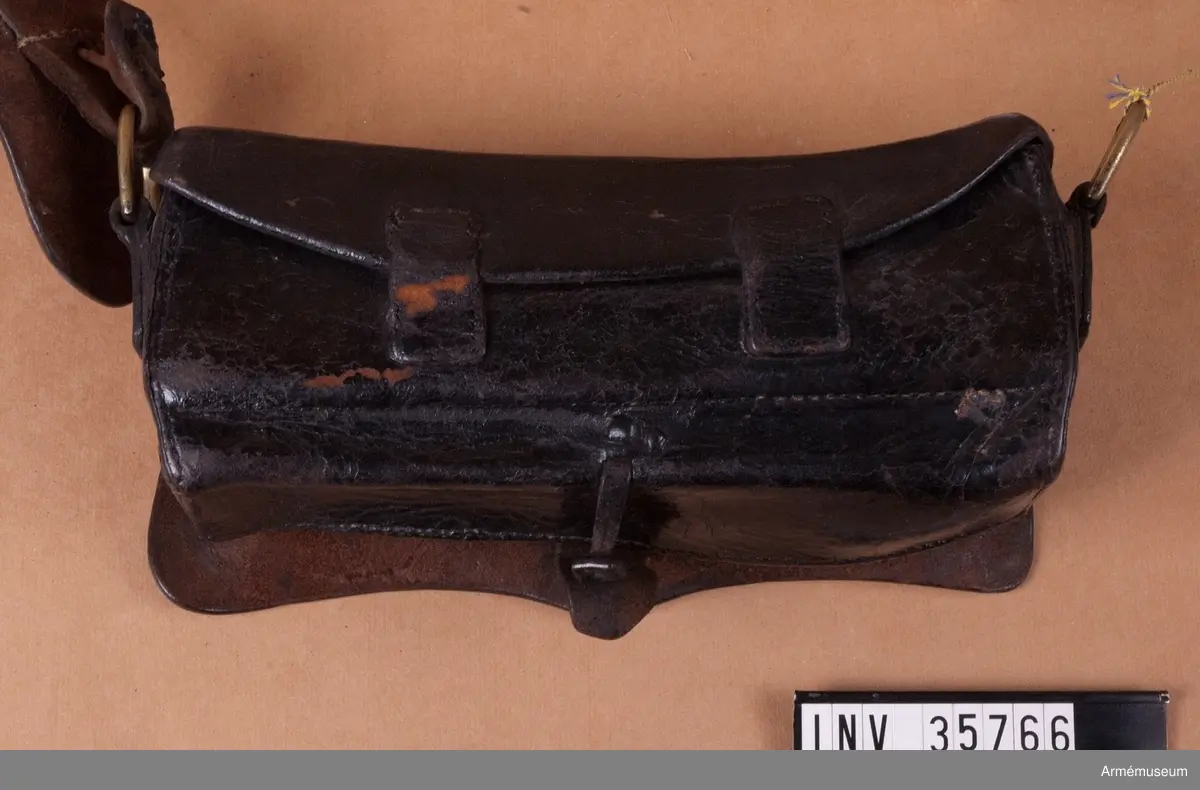 Kartuschväska av svart läder med mässingsbeslag i form av Skånes vapen. Kartuschen har en extra ficka för knallhattar och ett fack i botten som stängs med två remmar. De tillhörande spännena saknas. I kartuschen finns en träkloss med borrade hål med ca 18 mm diameter.
