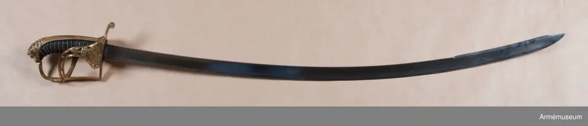 Klingans bredd upptill: 30 mm.Klingan är krökt, skålslipad och har nedtill en svart  betonad, tveegad klack. Fästet är av förgylld mässing. Kaveln är klädd med svart skinn en spiralräffla 16 varv. I bottnen på denna räffla är en av två parter hopsnodd, tunn mässingtråd anbringad. Baktill har kaveln ryggbeslag, som upptill övergår i en kappa, vilken är ciselerad i form av ett lejonhuvud och på vilken sitter en liten nitknapp. Parerstången är en rak och har fyrkantigt tvärsnitt samt av- slutas baktill av en nedböjd, på sidorna med ett spiralornament prydd knapp. Från parerstången främre ände utgår handbygeln i rät vinkel. Handbygeln är längs mitten litet försänkt och har längs var och en av framsidans kanter en ingraverad rand. Litet framför kappan genombrytes den av ett runt hål, och kring detta hål finns ciselerade ornament vilka bilda en stiliserad krans. På yttersidan finnes en uppåtböjd, delvis genombruten parerplåt, som är prydd med krönt sköld med tre kronor, vilken sköld omgives av ett par palmkvistar, allt i ciselerat arbete. Från parerplåtens spets utgår en delvis genombruten och sparsamt med ciselerade ornament prydd S-formig spång, som går till hand- bygelns övre del. På innersidan finns en liknande men mindre, ej genombruten och ej ciselerad parerplåt, från vars spets en S-formig spång går till handbygeln, vilken den träffar något längre ned än ytter- spången. Innerspången prydes längs kanterna av ingraverad rand.