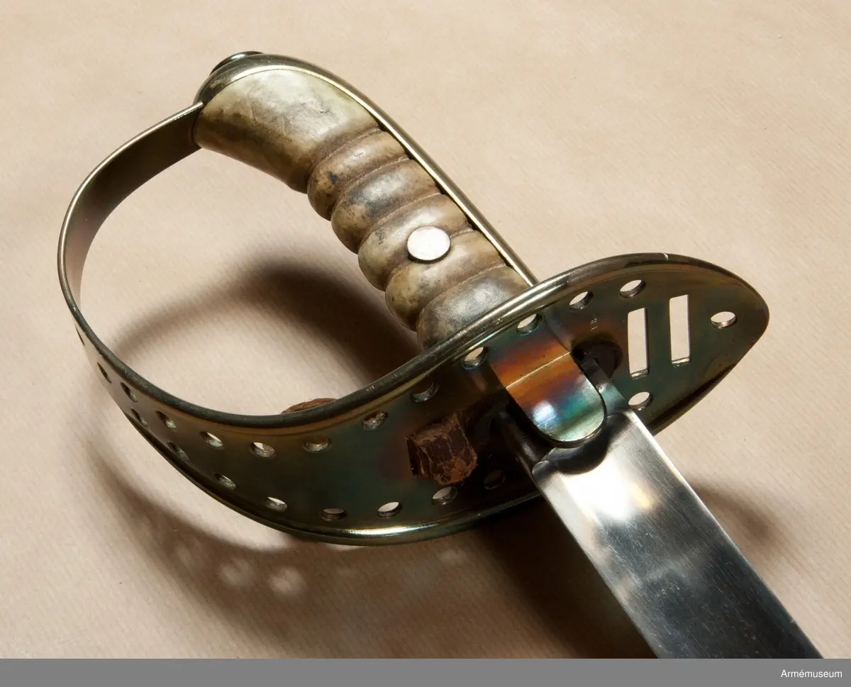 Klingan är till större delen av sin längd eneggad och skålslipad, men blir mot udden tveeggad och får ryggar. Klingbredd upptill: 31 mm. 

Fästets beslag är av mässing. Kaveln är klädd med vitaktigt läder och har sex räfflor. Genom den tredje nedifrån går en nit genom kaveln. Baktill har kaveln ryggbeslag, som upptill övergår i en avrundad kappa. På kappans översida finns en ganska stor, oval nitknapp. Nedtill går ett ringliknande mässingsbeslag kring kavel och ryggbeslag. 
Parerplåten är på det bredaste stället 9 cm. bred. Framtill slutar den i en liten snibb, som är lindrigt nedåtböjd. På undersidan är parerplåtens kanter förhöjda, men dessa förhöjningar slutar baktill en liten bit från den ovan omtalade snibben och fortsätter framtill in på handbygelns nedersta del. Framför kaveln finns två horisontala springor för handremmen och bakom kaveln genombryts parerplåten av två liknande springor för handremmen. Längs parerplåtens kanter, från springorna för handremmen till något under handbygelns mitt, finns vid varje kant 11 runda hål. Ovanför det översta hålparet sitter två hål i rad och längs bak, bakom springorna för handremmen, sitter ett ensamt hål. Från parerplåtens undersida går ett par rätt breda, nedtill avrundade styrskenor ut nedåt. På parerplåtens undersida bakom klingan står J. S. och F. B. 

Enligt anmärkning i 1888 års tryckta katalog skiljer sig detta vapen från projektmodellen, AM 39853, genom att fästet är rymligare.