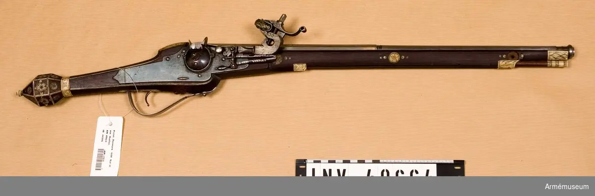 Grupp E III.
Pistolen är fullkomligt lik AM 40663, utom i att längs varbygelns undersida går en ingraverad rand. Dessutom har laddstaken, som även här är av trä med skoning av gravarat ben, i smaländan ett 9.5 cm långt järnbeslagen, i vilket finnes ett gängat hål för en krats. Den framtill på framstockens högra sida befintliga graverade benskivan med hål för främre pipsitift är utfallen.