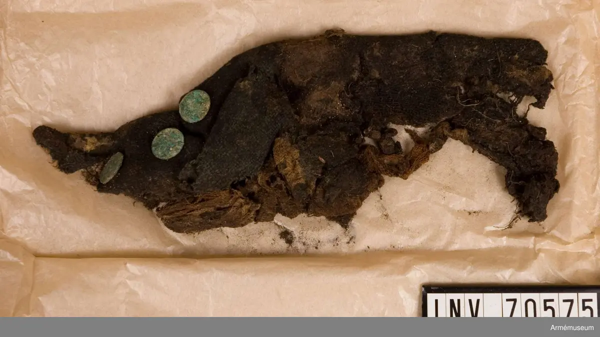 Grupp C:I. 
Funna vid grävningar sommaren 1939. Gravfynd från Sandhamn bestående av knappar och tygrester