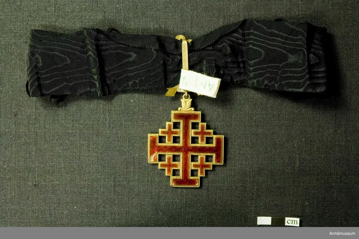 Påvliga Heliga Gravens orden, kommendörstecken i svart band. 
Miniatyr och knapp. Ordenstecknet i form av pilgrimssnäcka tilldelades ordensriddare som genomfört en pilgrimsresa till det heliga landet.

Förvaras i samhörande etui.