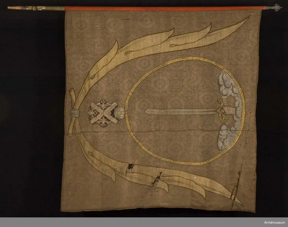 Duk av brun kinesisk sidendamast. Dekor i intarsia och målade detaljer. Motivet föreställer en hand med svärd som kommer ner ur ett moln omgivet av andreasordens kedja med dess insignier nedtill. Det hela omgivet av nedtill korslagda palmkvistar.
Slät, grönmålad stång. Spetsen bevarad.