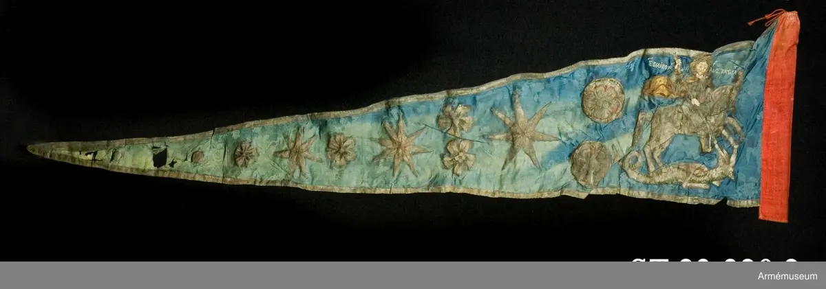Entungad lansfana. Duk av blå kinesisk sidendamast med målad dekor. I 1703 års inventarium anges motivet vara St Göran men enligt den ryska inskriptionen är det Feodor Stratilat . Rosor och stjärnor av silver. Duken kantad med en silverbård. Strumpa av rött linne.