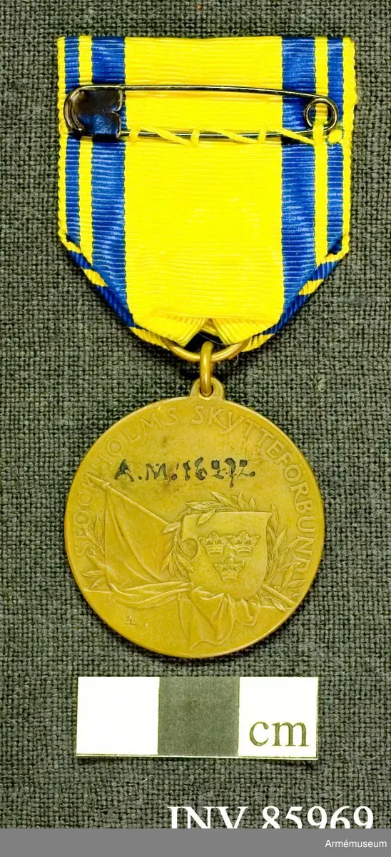 Grupp M. 
Åtsidan: Medaljen som saknar ytterrand, visar en stående kvinna, framåtvänd, i nästan helfigur, med bart huvud, i veckad dräkt och mycket vida ärmar, med den högra handen framräckande ett gevär, varav översta delen av pipan och nedesta delen av kolven på grund av medaljens rundning icke synas. Venstra handen, stödd på ett postament, håller en lagerkrans. Mellan figuren och geväret läses i upphöjda bokstäver: FÖR FOSTERLANDET, på 3 rader. Bakom skymtar en del av en flaggstång och en delav en fladdrande flagga. På postamentets framsida 3 1910. 
Frånsidan:  STOCKHOLMS SKYTTEFÖRBUND. Från medaljens mitt och nedåt är lagd en sköld med Sveriges tre kronor och omvirad av en lagerkvist; bakom skölden står, lutad snett upp mot venster en fanstång med en fana, stiliserat hängande på och nedanför avskärningen. På avskärningen: 3. Å medaljens översida är anbragt en ögla, vari medelst en ring är fäst ett 35 mm brett gult, vattrat ripsband med å vardera sidan två blå kanter, en bredare innest och en smalare ytterst.
Beskrivning: C.P.
