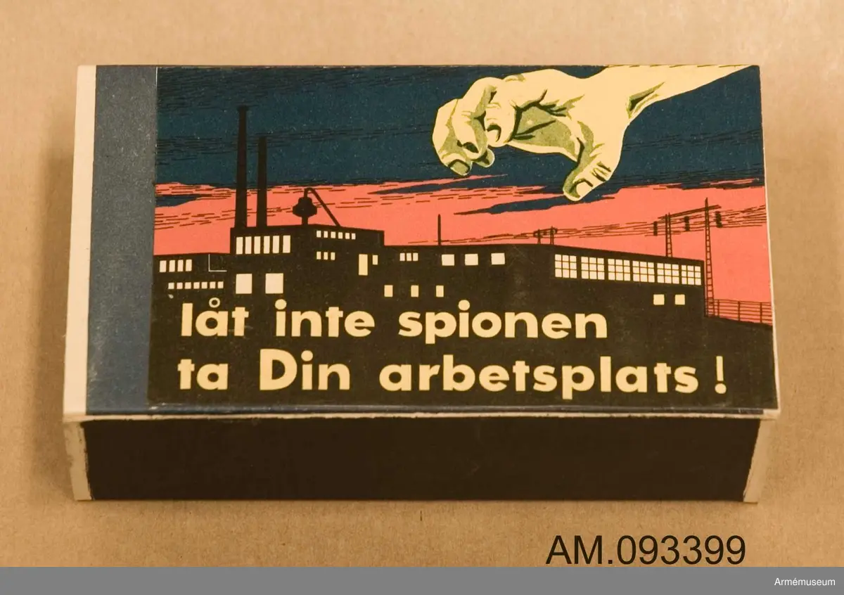 Tändsticksask med tändstickor. På ena sidan motivet Tre stjärnor och på andra sidan ett klistermärke med motivet en spionhand sträcker sig över en industribyggnad nattetid.