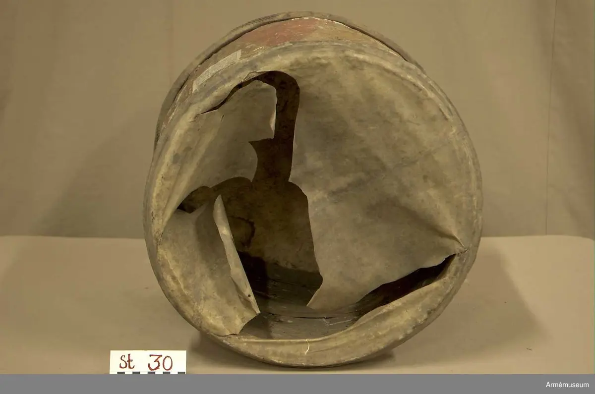 Cylindertrumma av: trä därpå spänd lim o krita grunderad duk som är bemålad. Hål i olika storlek, i jämn rad efter hela sidan. Svårt att säga stick eller insekts hål. Dessutom 7 st. hål i olika storlek, placerade runt om på cylindern. Till höger om den klistrade etiketten finns en stor ruta ca 8x7 cm. med ett totalt bortfall av kredering. För övrigt är ytan mkt. krackelerad och ostabil. 

Membran : övre skinnet är trasigt, undre skinnet är fogat efter spännringen och vågigt.

Veckelgjordar: saknas.

Spännlina: saknas. 

Spännringar : två stycken.

Utsmyckning : bemålad med röda kilar på gul botten. Ristat mönster. 

Märkning : klistrad färdigtryckt Konung Carl den XII etikett med ifyllnad
Litt. B. -No 25.