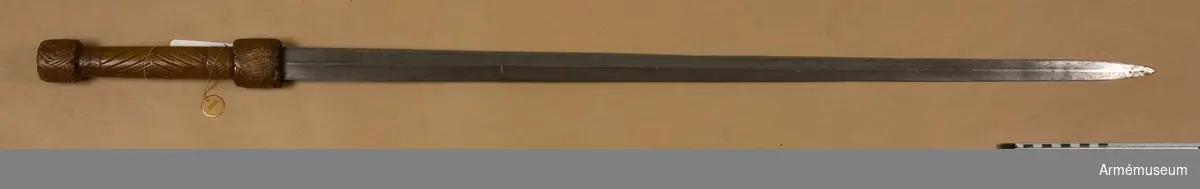 Värjkäpp, "stav med lönnvärja", tillverkad av en runstav med kalenderrunor. Baljan består av runstavens nedre del med kalenderrunor.
Klingans bredd upptill är 38 mm. Klingan är tveeggad med ryggar. På klingans ena sida är omkring 130 mm nedanför fästet ett par pilliknande stämplar inslagna. På samma sida, 240 mm nedanför  fästet, syns tydliga rester av en djurfigur, formad av inhuggna, med mässing inslagna streck. Denna figur är tydligen "ulvmärket", som ursprungligen användes av smederna i Passau, men som på 1400-talets slut samt på 1500- och 1600-talet imiterades lite varstans.
Fästet, eller handtaget, är långt samt har upp- och nedtill hjaltliknande förstärkningar, som pryds med inskurna flätornament. Bägge förstärkningarna har svagt ovalt tvärsnitt. Den övre förstärkningen är 40 mm och den nedre, vars kant skjuter ut över baljans övre kant, är 50 mm lång. Också kaveln har svagt ovalt tvärsnitt samt är prydd med inskuren, enkel ornamentik.

Vid tillverkningen av denna värjkäpp har man använt en vanlig runstav. Hopsättningen är troligen från 1600-talets början eller förra hälft, men klingan, som tydligen var bredare, men avslipats, kan gott vara äldre.
Handtagets ornamentik är typisk för Uppland, medan gyllentalen i baljans kalenderrunor skulle kunna vara från Närke. Det är inte säkert att handtag och balja kommer från samma runstav.
Handtaget har en ytbehandling av bivax löst i terpentin, vilket var vanligt på runstavar.

I Livrustkammaren finns ett liknande "rundsvärd", vilket Gustaf II Adolf år 1615 erhöll som gåva av Johannes Bureus (se katalogen över Gustav  Adolfsutställningen 1932, no 55).
Jämför också Karl IX:s stav  med lönnvärja hos Livrustkammaren (inv LK 3836).