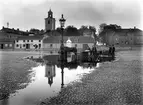 År 1924. Kanalen svämmar över vid Östra torget i Jönköping. Utmed Kanalgatan ligger Nya Hushållsaffären och Beklädnadsaffär. På taket finns en  reklamskylt: