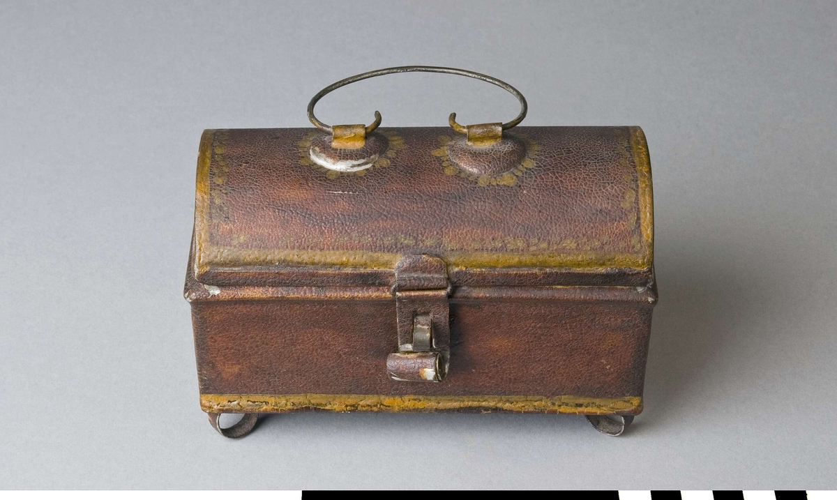 Reseschatull avsett för skrivdon, av bleckplåt. Modell som en liten kista, med kupigt gångjärnsförsett lock och fötter. Inredd med tre fyrkantiga fack och ett smalt som följer framsidan. Endast ett skrivdon finns kvar, en sandströare. På locket ett bygelformat handtag av ståltråd, med två fästen. Fällbar låstunga som passar till en bygel på lådans framsida. Inget lås finns kvar. Fötterna, en i varje hörn, är tillverkade av plåtringar. Schatullet är målat, troligen i rött eller brunt, med gula markeringar runt kanter och handtagsfästen.