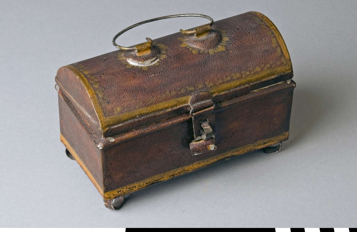 Reseschatull avsett för skrivdon, av bleckplåt. Modell som en liten kista, med kupigt gångjärnsförsett lock och fötter. Inredd med tre fyrkantiga fack och ett smalt som följer framsidan. Endast ett skrivdon finns kvar, en sandströare. På locket ett bygelformat handtag av ståltråd, med två fästen. Fällbar låstunga som passar till en bygel på lådans framsida. Inget lås finns kvar. Fötterna, en i varje hörn, är tillverkade av plåtringar. Schatullet är målat, troligen i rött eller brunt, med gula markeringar runt kanter och handtagsfästen.