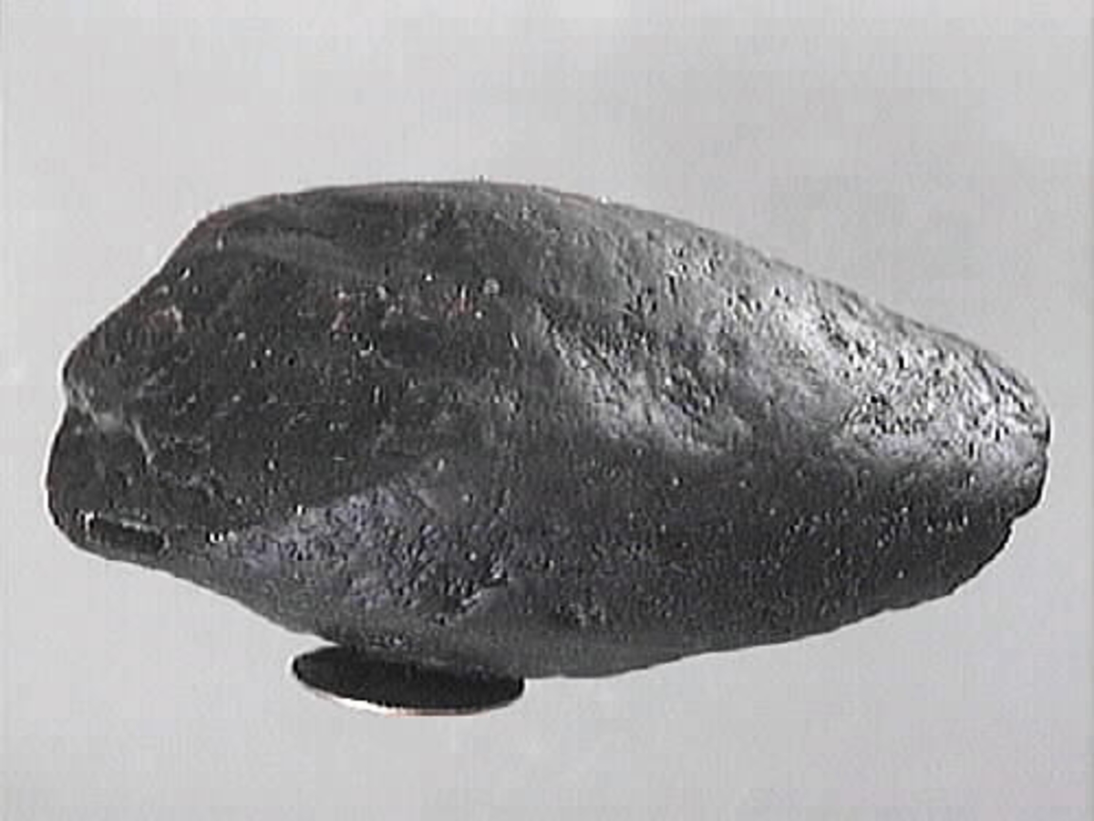 Del av arm till en skulpterad krigare. Oval form. Ovansidan är rundad. Baksidan är troligtvis bruten. Ena kortänden är bruten.
Skulpturdelen är mycket sliten.

Text in English: Part of sculpted arm of a warrior. Oval shaped. Slightly more rounded on one side, one end is broken. Much worn.